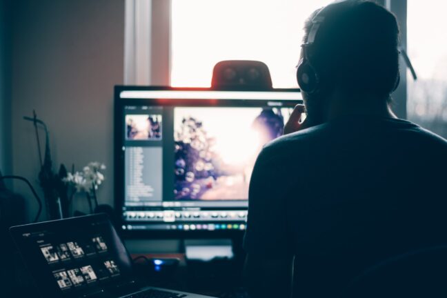 A man with headphones sitting in front of a monitor at a desk editing a photo with Lightroom Classic.
